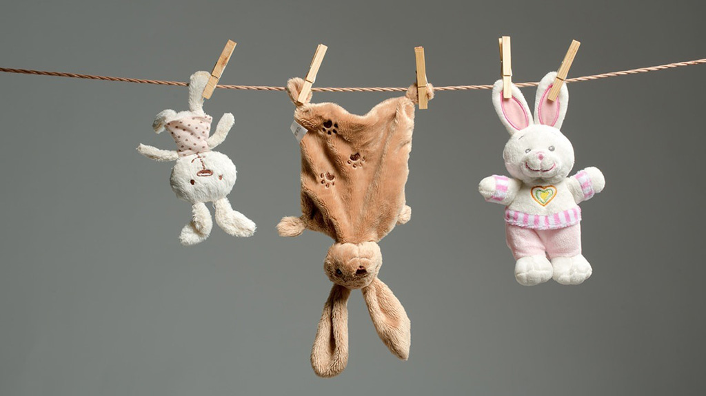 Three plush bunny toys hanging on a clothesline with clothespins after washing, showing proper cleaning and drying care for stuffed animals.