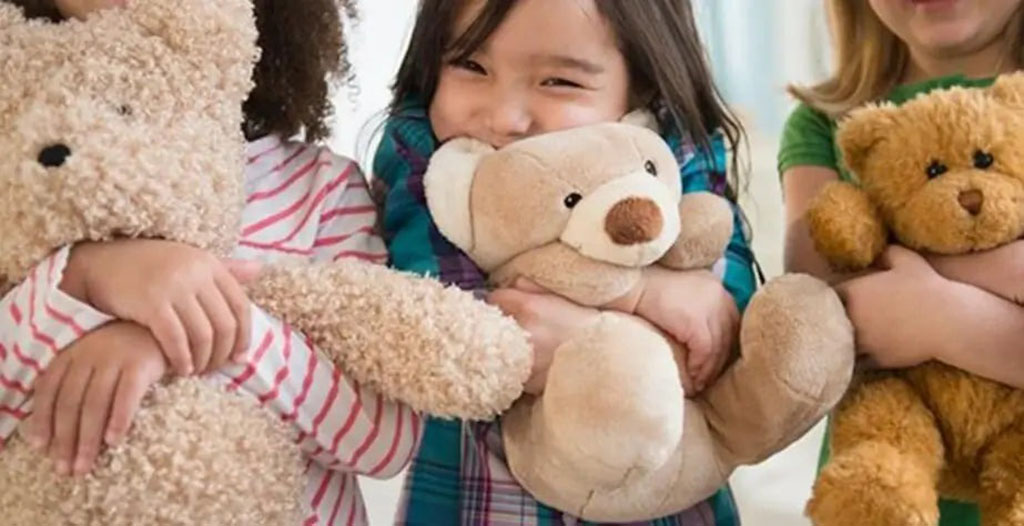 Three smiling children hugging soft teddy bears of different colors, showing affection and joy while playing together.