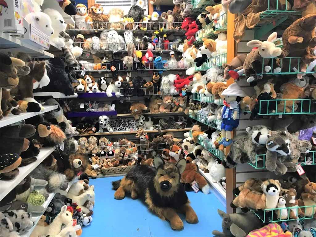 Shelves filled with various plush animals, including dogs, owls, and bears, with a large German Shepherd plush in the center of a toy store display.