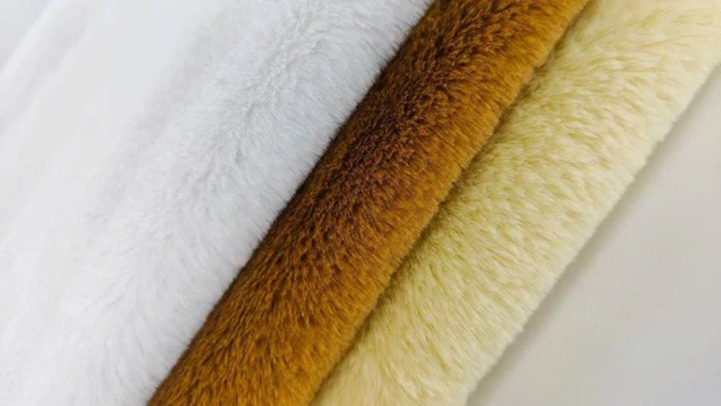 Close-up view of soft faux fur fabric rolls in white, brown, and cream colors used for plush toys and garments.