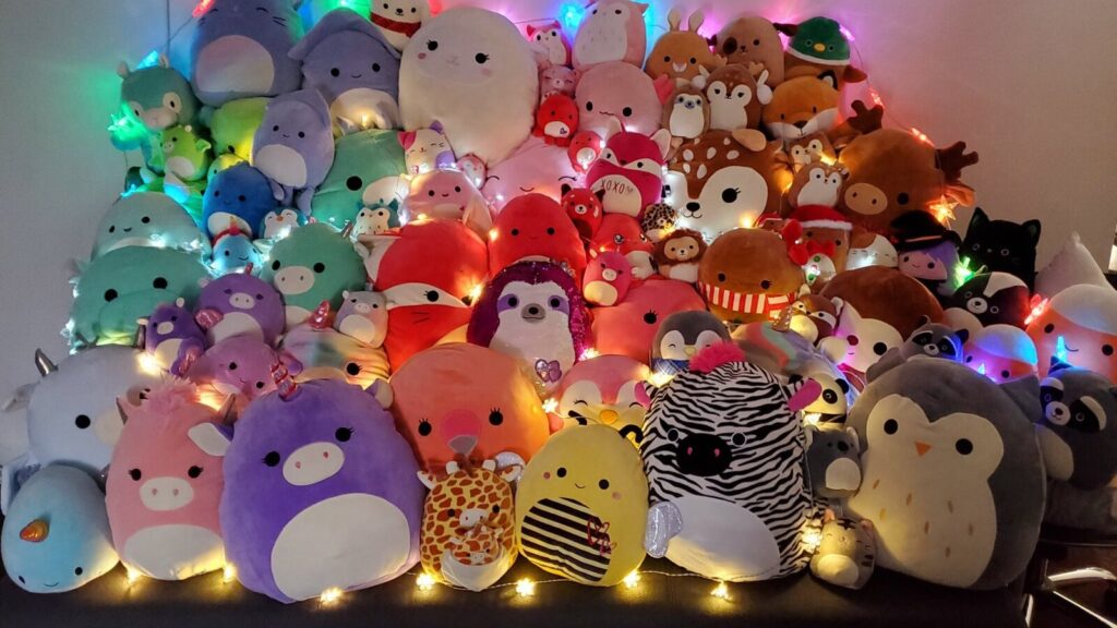 A large colorful display of Squishmallows plush toys of various animals and characters decorated with string lights.