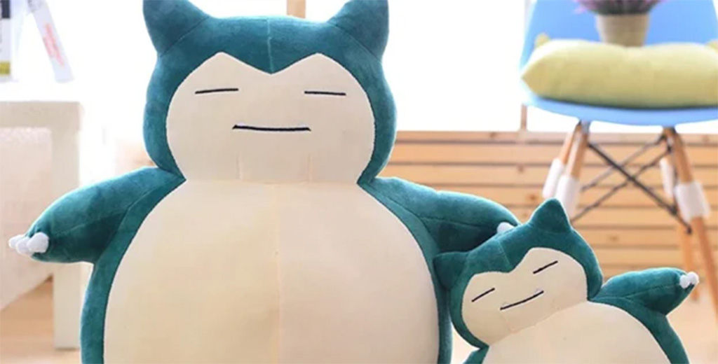 Two teal and cream-colored plush toys, one large and one small, sitting side by side in a cozy room with soft lighting and wooden decor.