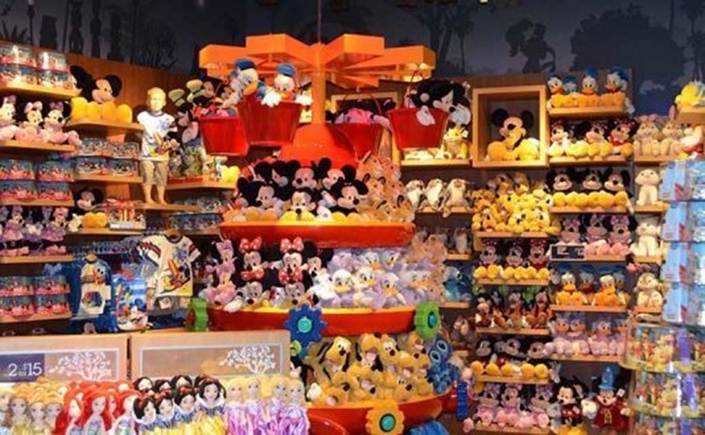 Shelves filled with Disney plush toys including Mickey, Minnie, Donald, and princess dolls in a colorful retail store display.