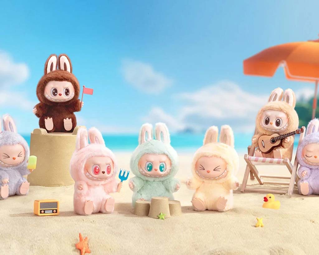 Cute Labubu plush toys dressed in bunny suits playing on the beach with sandcastles, a guitar, and popsicles under a bright blue sky.
