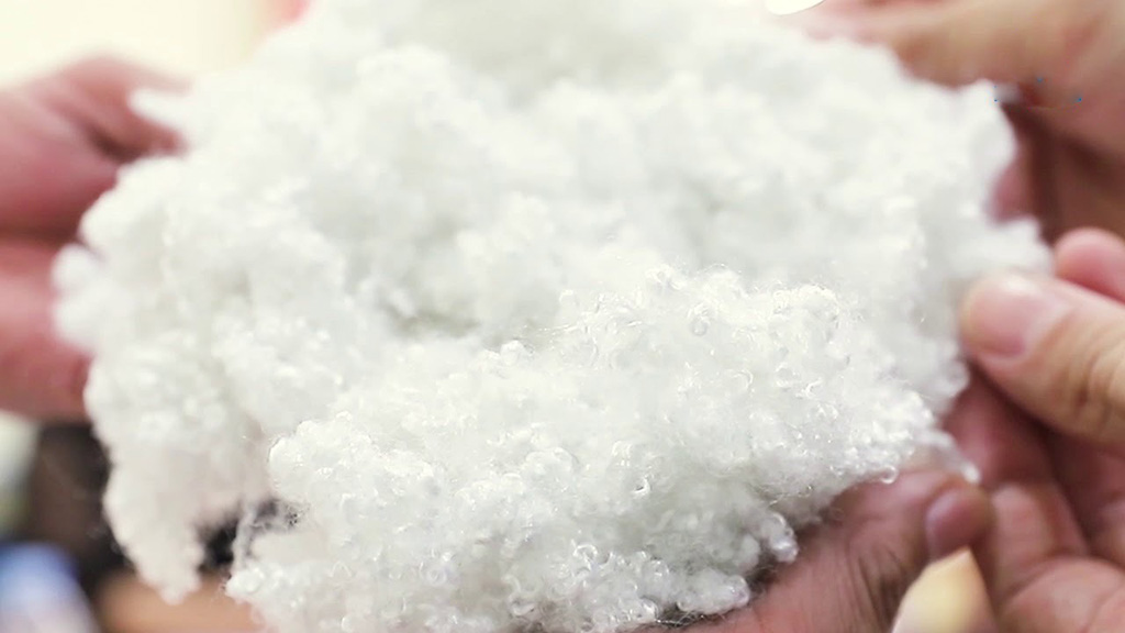 Close-up of hands holding fluffy, curly white polyester fiberfill used as stuffing material for plush toys and cushions.