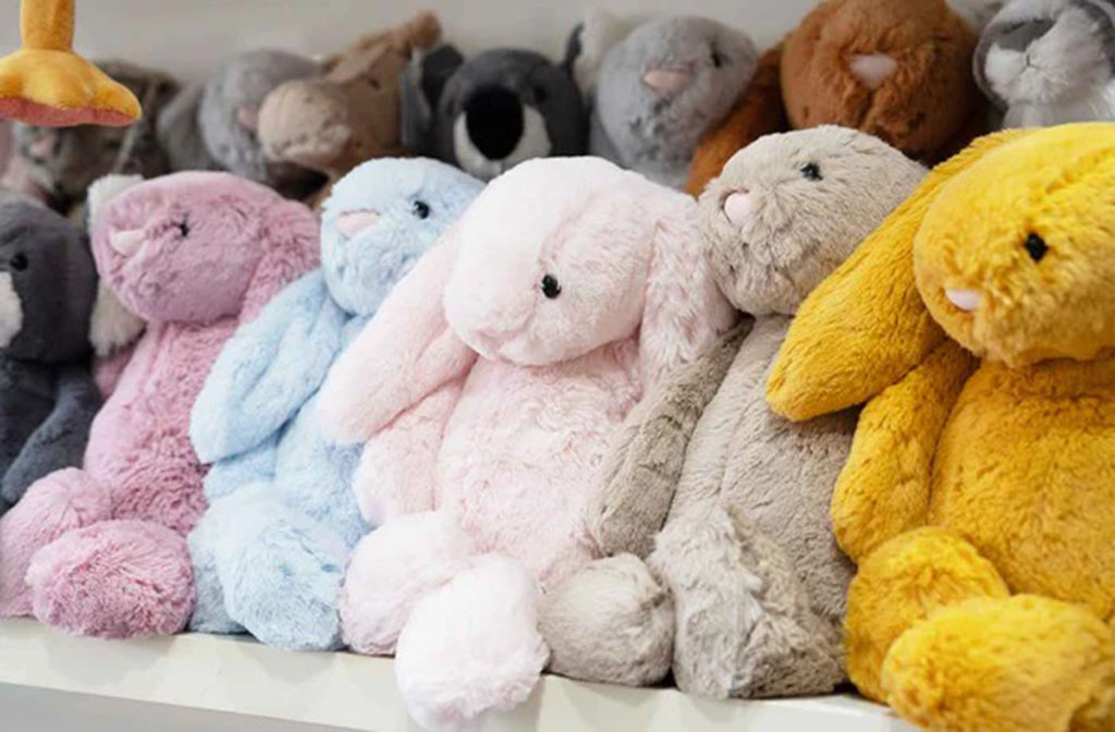 A row of colorful plush bunnies in pastel shades of pink, blue, grey, and yellow displayed neatly on a shelf.