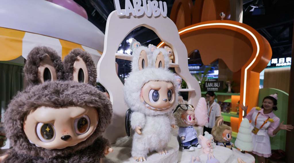 Large LABUBU figures and smaller character dolls displayed at a Pop Mart exhibition booth with staff in the background.