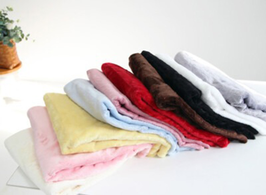 Stack of colorful plush fabric rolls in pastel and dark shades neatly folded on a white table.