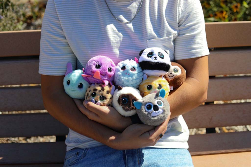 Person holding a group of small Ty Beanie Boos plush toys, including animals like pandas, owls, and unicorns, on a bench outdoors.