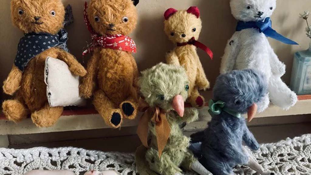 A collection of handmade vintage-style plush animals, including bears and birds, made from mohair fabric with scarves and ribbons, displayed on a shelf with lace decoration.