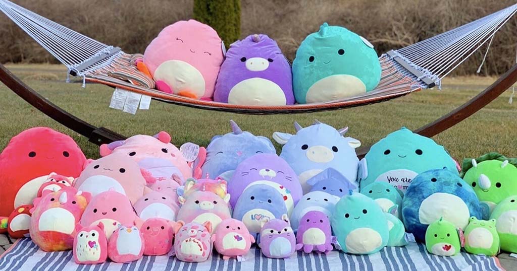 Assorted colorful squishy plush toys in various sizes and animal shapes displayed outdoors on a hammock and blanket.