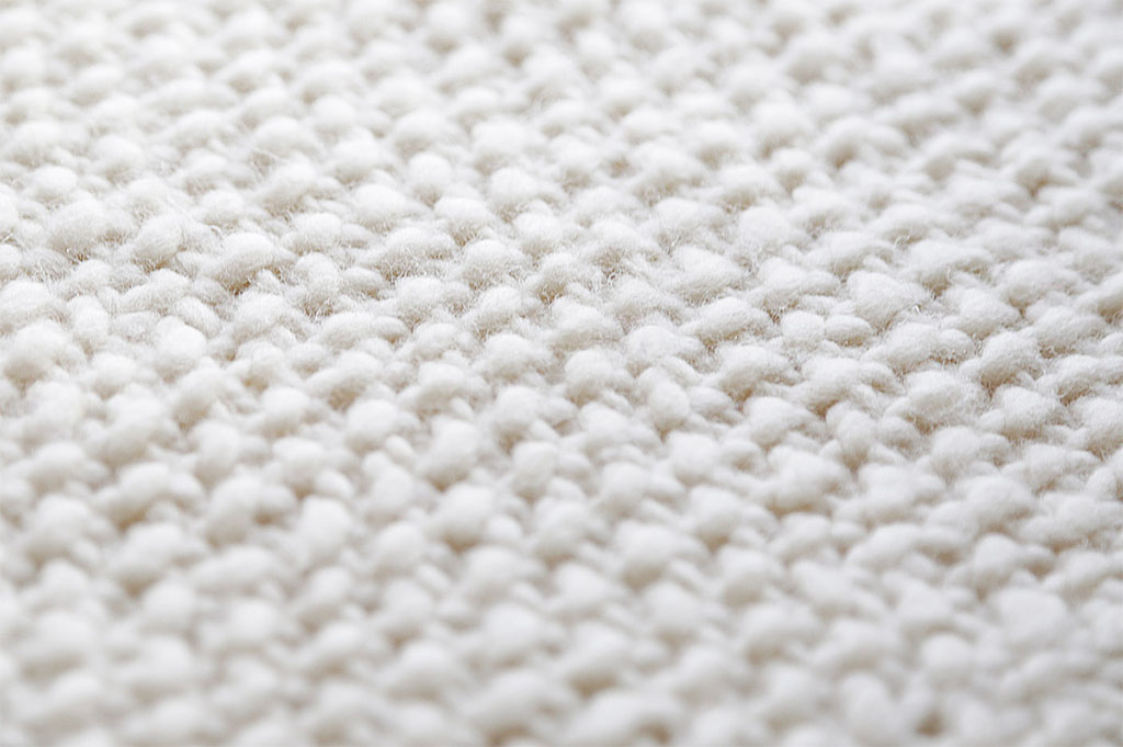 Macro photo of soft white wool fabric showing its woven, fluffy texture used in sustainable textile production.
