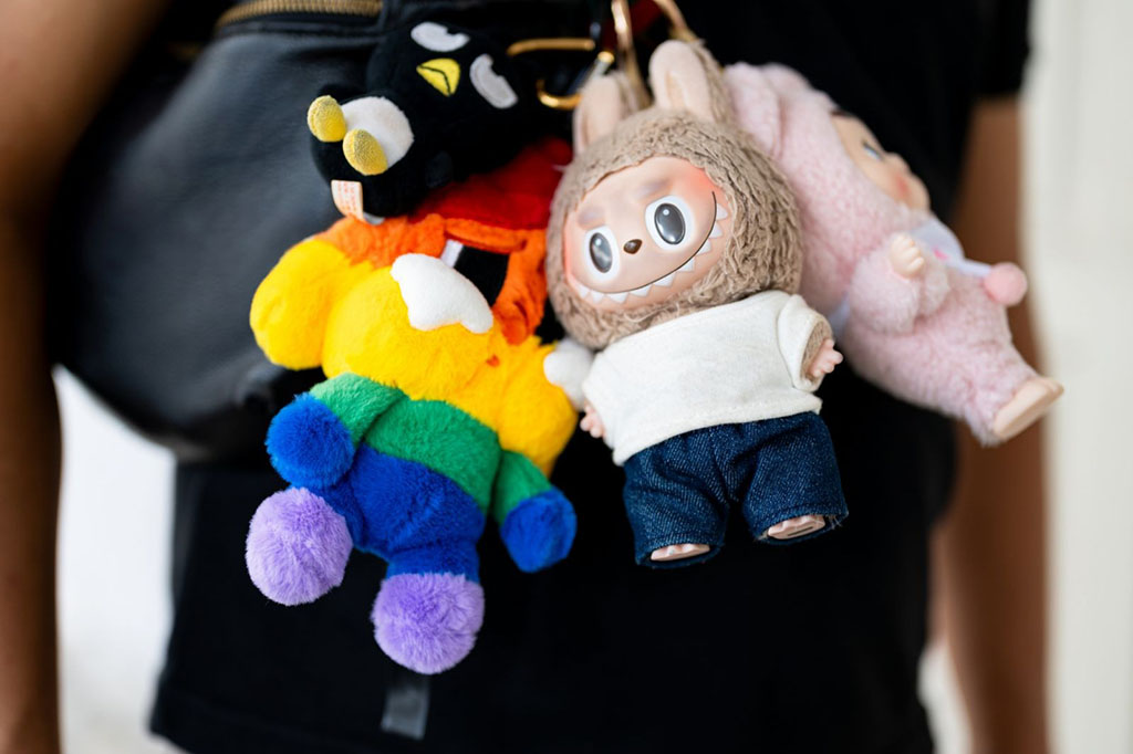 Close-up of colorful plush keychains attached to a black bag, including cute doll and animal designs in various vibrant colors.