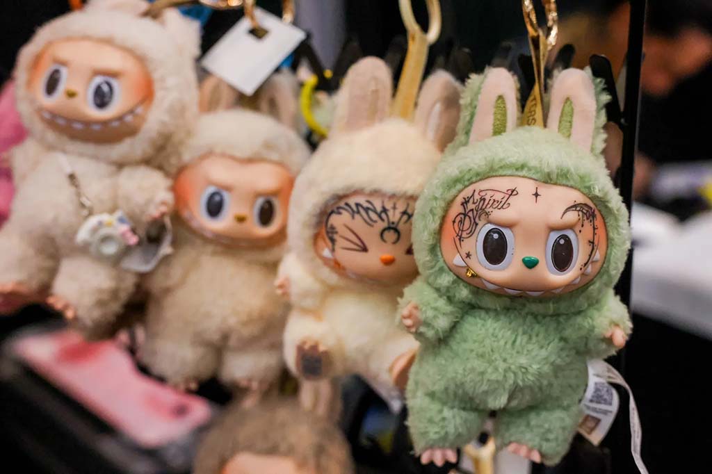 Cute plush keychain dolls with large expressive eyes and fluffy animal costumes, including green and beige bunny outfits, hanging on display.