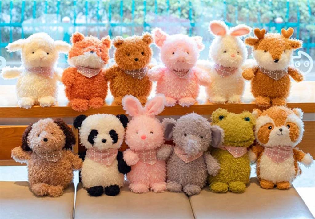 Group of colorful fluffy plush animals including bunnies, foxes, bears, and pandas displayed on wooden shelves indoors.