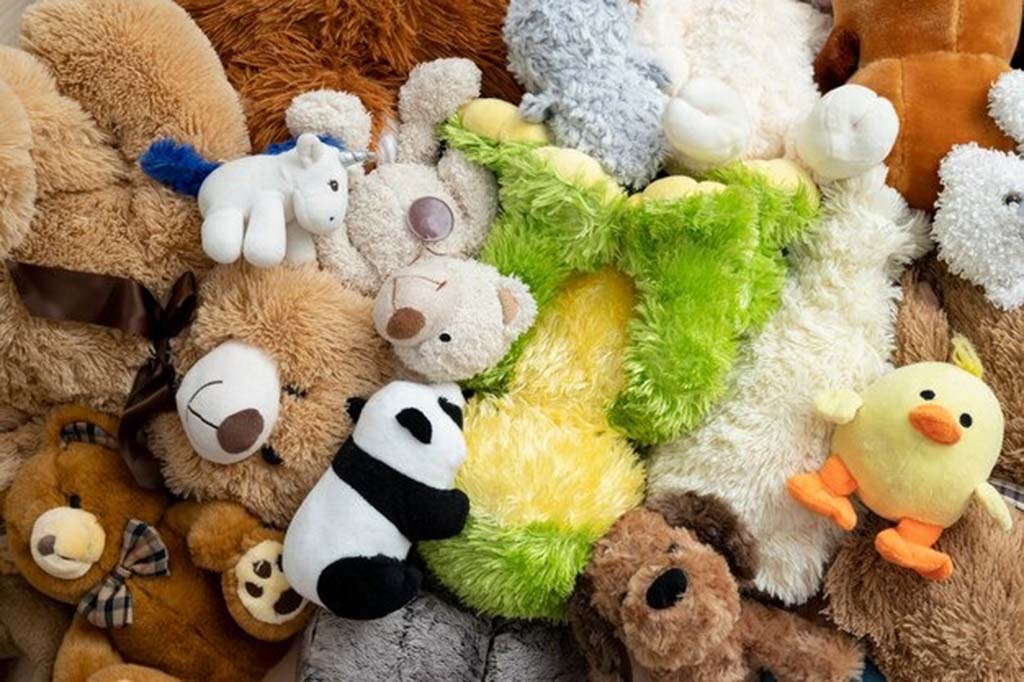 Close-up view of a pile of various plush toys including teddy bears, a panda, a duck, and a unicorn, showcasing different soft textures and colorful fabrics.