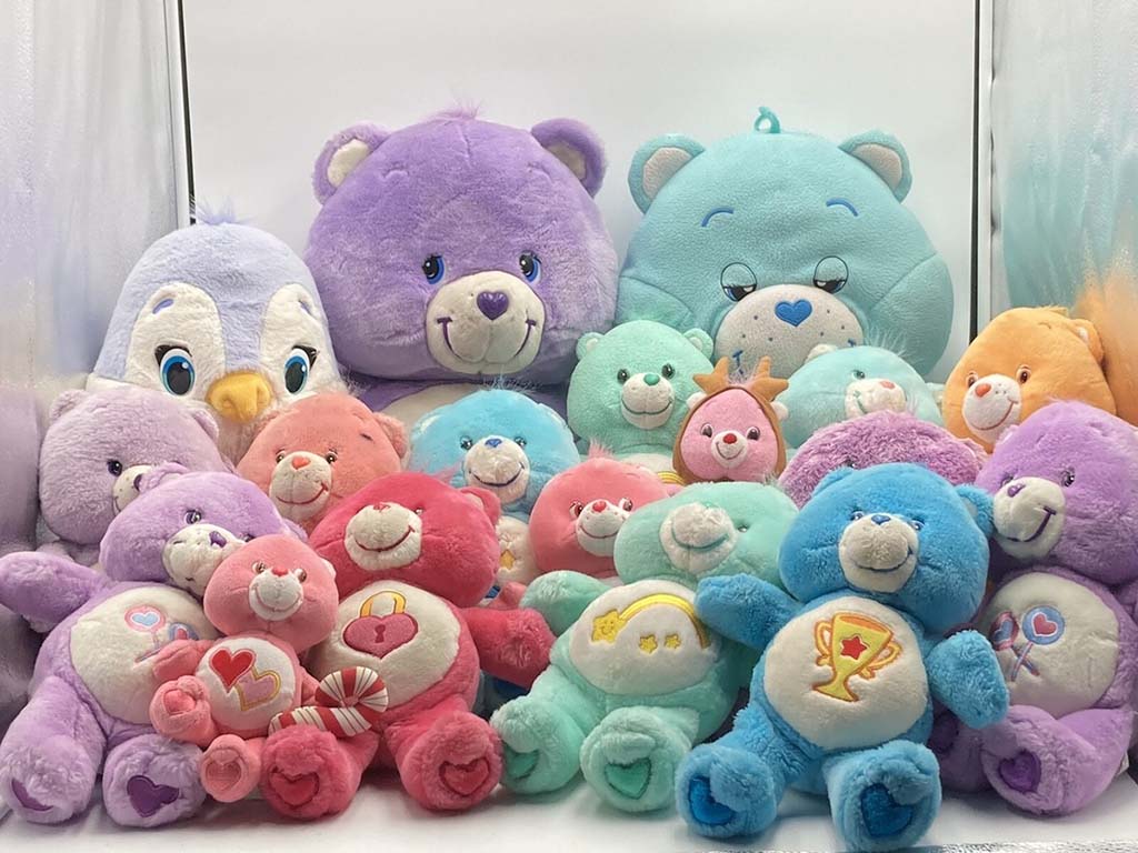 Group of colorful plush teddy bears in pastel shades including blue, pink, purple, and mint, arranged together in a display case.