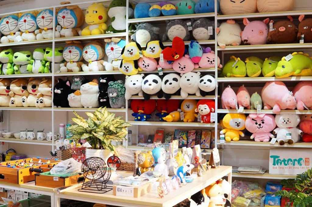 A brightly lit plush toy store with colorful stuffed animals, cartoon characters, and gift items neatly arranged on white shelves and display tables.