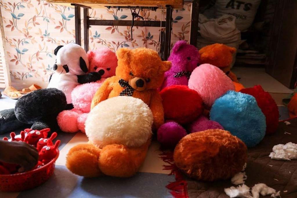 A group of colorful teddy bears and stuffed animals in various stages of completion inside a small plush toy workshop.