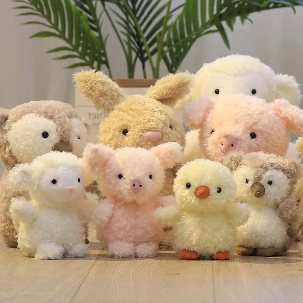 A group of small, fluffy plush toys including a chick, bunny, pig, owl, and lamb, arranged together on a wooden floor with a plant in the background.