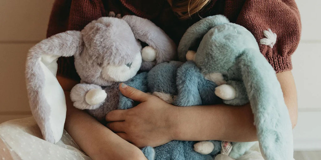 Close-up of a child hugging three soft bunny plush toys in pastel colors—purple, blue, and teal—showing comfort and affection.