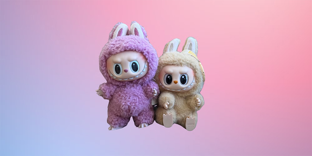 Two Labubu plush toys wearing fuzzy bunny costumes, one in purple and one in beige, displayed against a soft pink and blue gradient background.