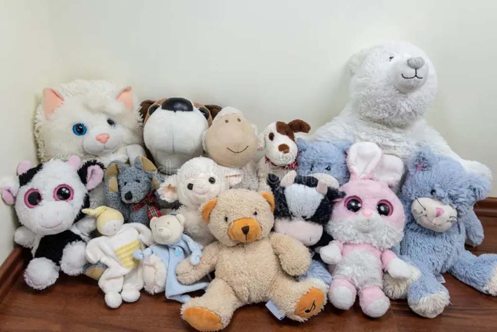 Collection of assorted plush toys including bears, rabbits, and cats arranged on a wooden floor.