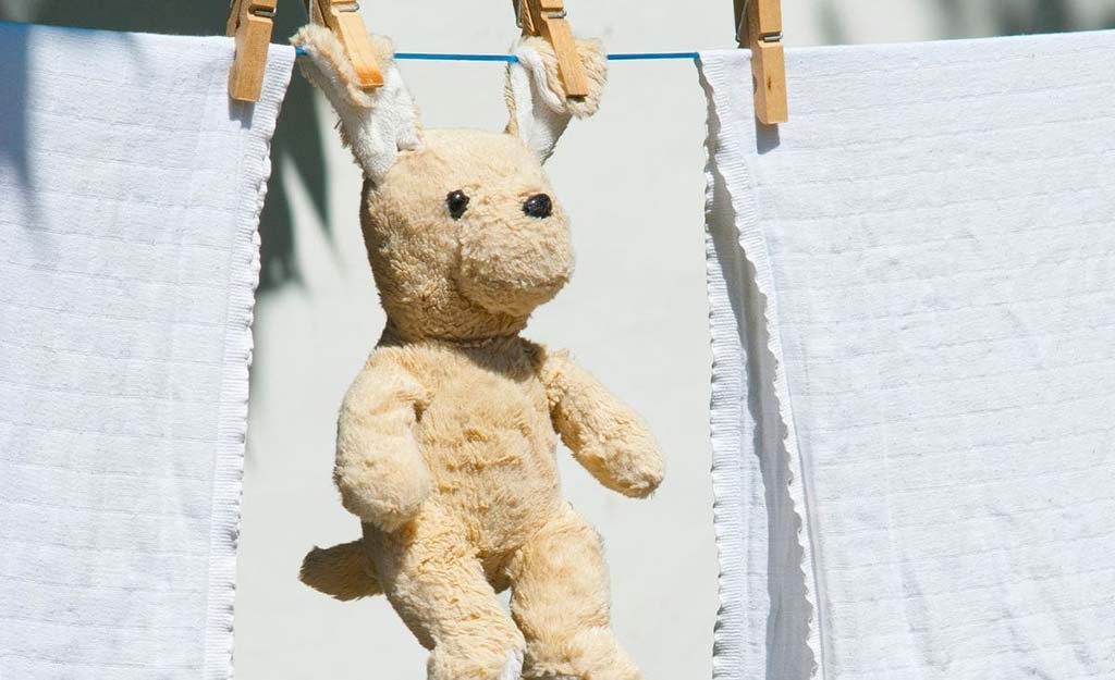 Clean plush toy hanging on a clothesline with clothespins between two white towels under sunlight.