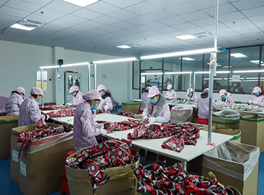 Factory workers wearing uniforms and masks conduct quality inspection on patterned plush fabric pieces under bright lighting in a clean workshop.