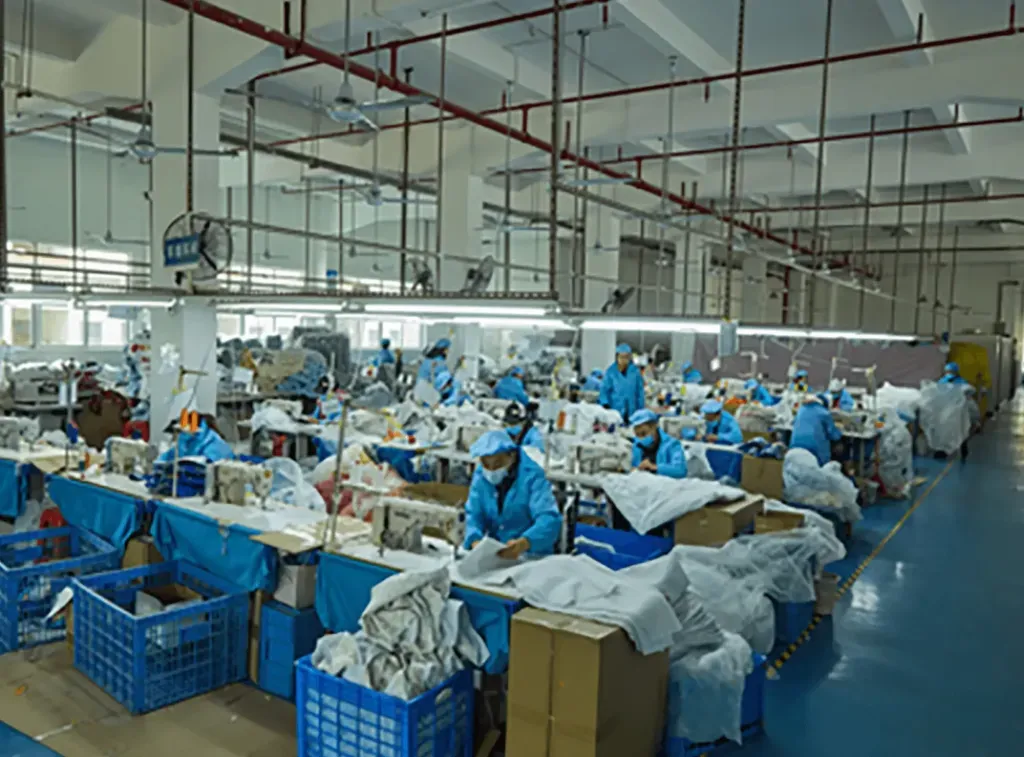 Factory workers in blue uniforms sewing and assembling plush toys at organized workstations along a production line.