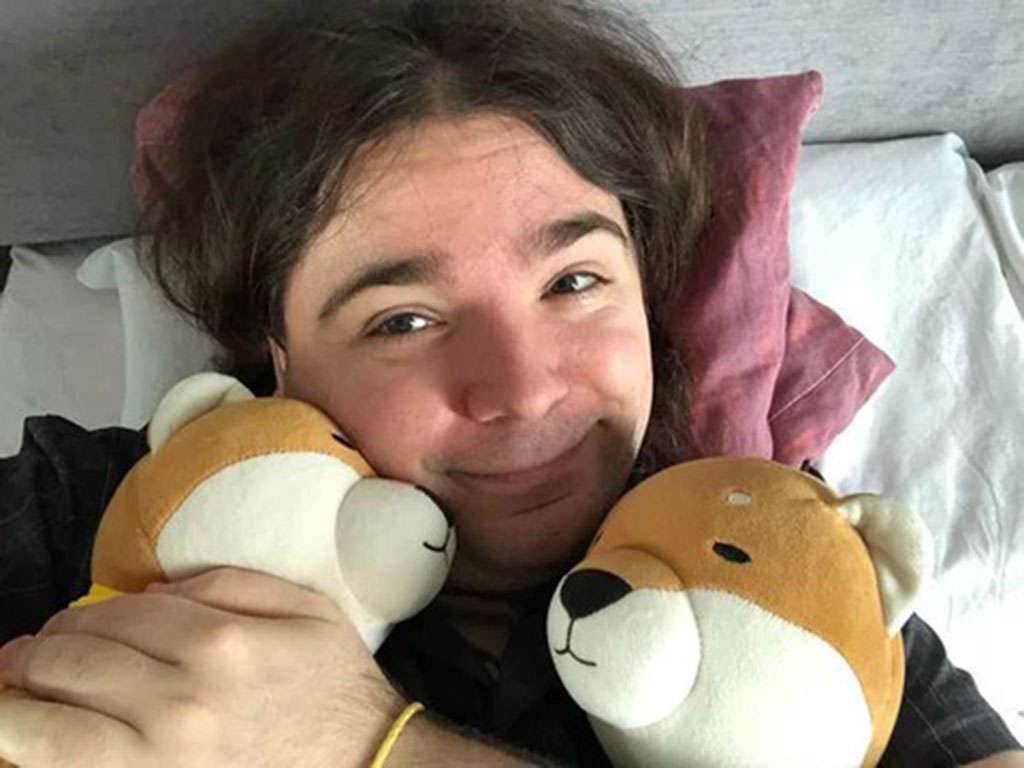 Person lying on a bed smiling while hugging two soft plush dog toys for comfort and relaxation.