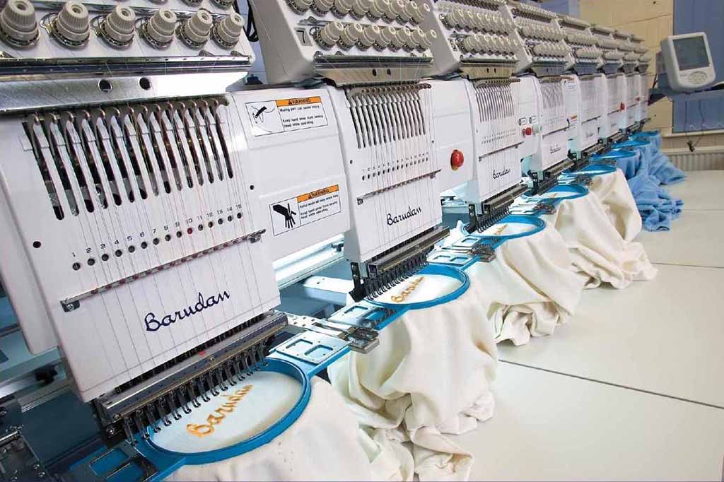 Row of computerized embroidery machines stitching designs onto fabric, used for creating detailed plush toy faces and logos.