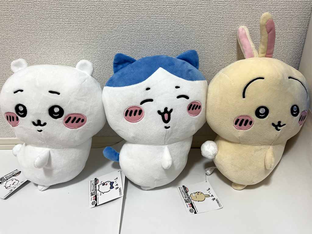 Three adorable plush toys with blushing cheeks and expressive faces, featuring a white bear, a blue-eared cat, and a beige bunny on display.