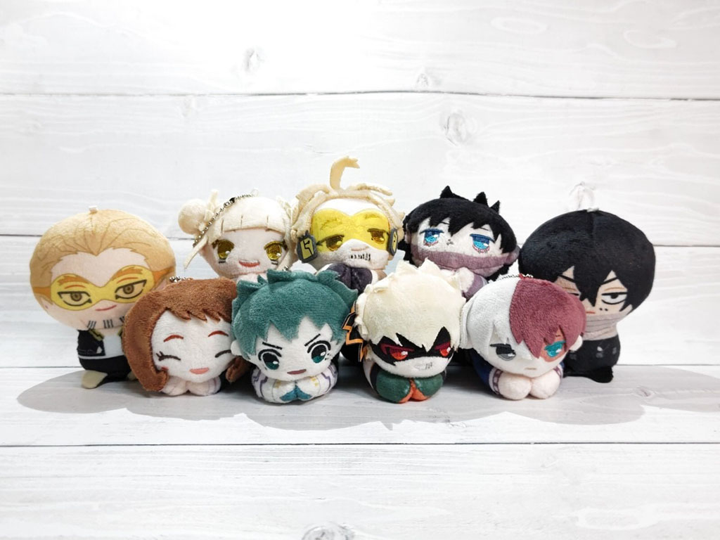 A collection of small anime-style plush keychains featuring various colorful characters arranged in two rows on a light wooden surface.