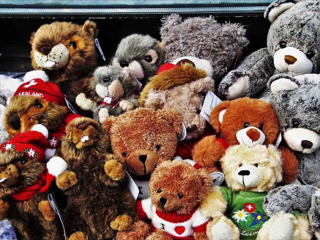Pile of colorful plush teddy bears wearing festive clothes and accessories displayed together for sale.