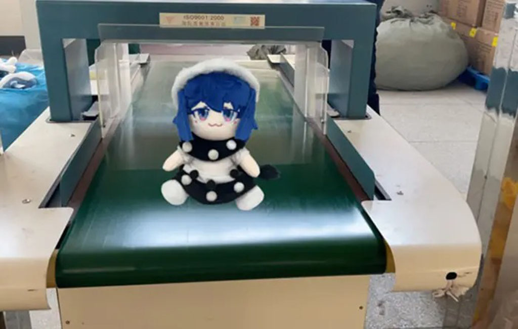 Plush doll with blue hair on conveyor belt passing through a metal detector for safety inspection.