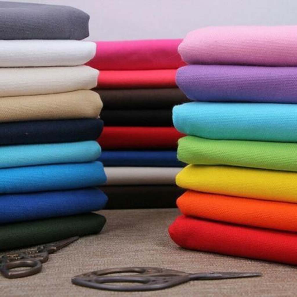 Two stacks of neatly folded plain-dyed fabrics in various bright and neutral colors placed on a table with sewing scissors.