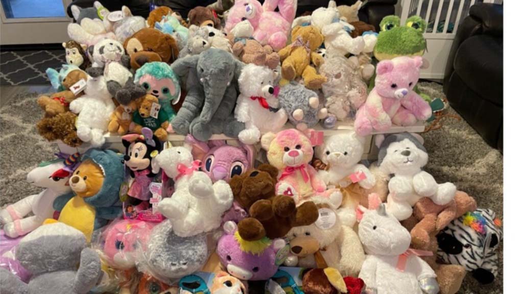 A colorful assortment of plush toys including teddy bears, elephants, unicorns, and cartoon characters piled together in a cozy indoor setting.