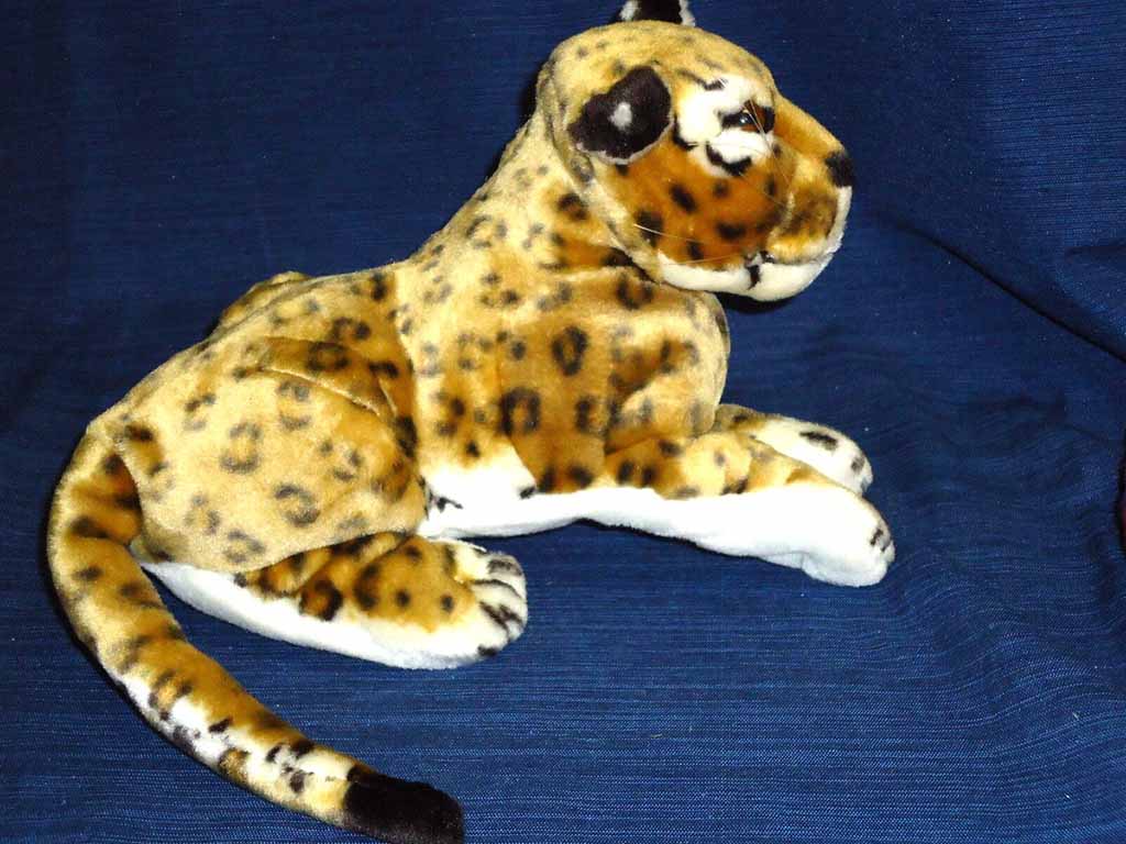 Realistic leopard plush toy with spotted fur lying on a dark blue background.