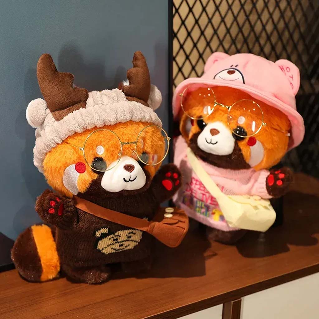 Two red panda plush toys wearing glasses, cozy clothes, and hats—one in a brown sweater with antlers and the other in a pink outfit with a bear hat.