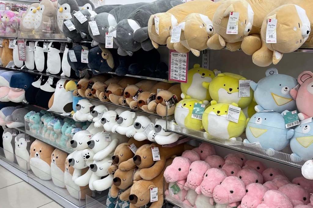Shelves filled with various plush toys in different colors and shapes, including animals and round characters, neatly arranged in a retail store.