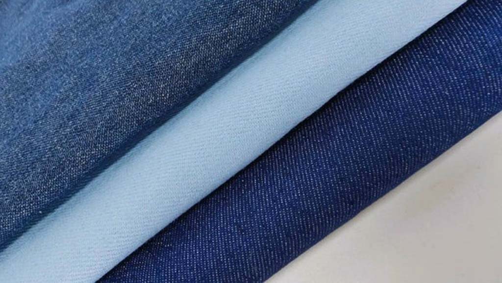 Folded layers of denim fabric in light and dark blue shades showing the texture and weave pattern clearly.