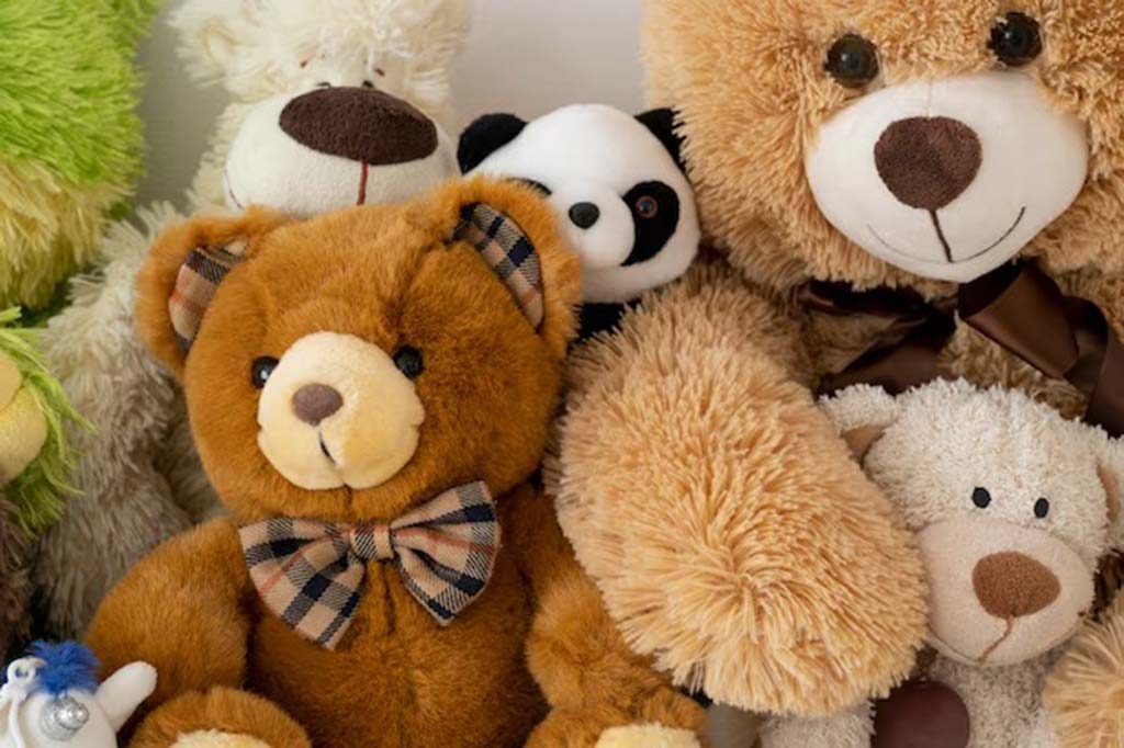 Close-up of various plush teddy bears in different colors and sizes, including a brown bear with a checkered bowtie and a panda toy in the background.