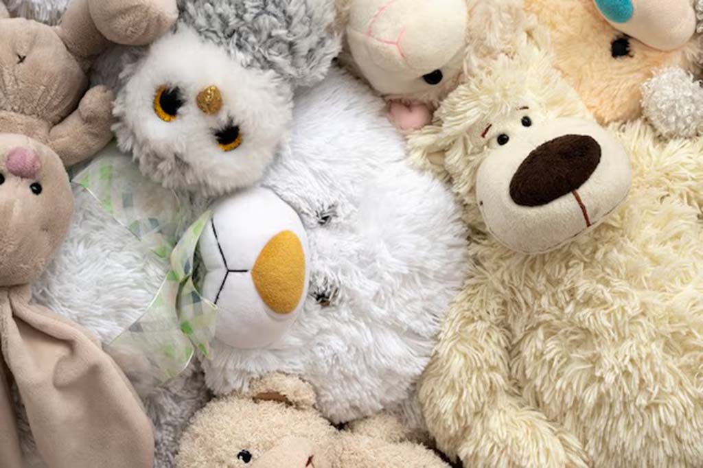 A close-up view of various plush toys including a fluffy bear, owl, bunny, and dog, all made from soft textured fabrics in neutral tones.