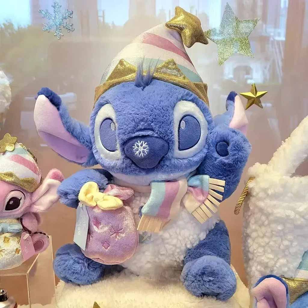 A cute blue plush toy wearing a pastel scarf and gold-trimmed party hat, holding a small gift bag, surrounded by festive decorations and stars.