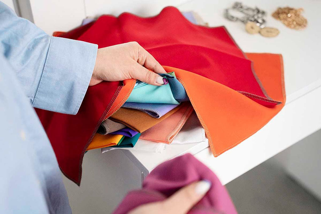 Person holding colorful fabric swatches in red, orange, blue, and brown tones, selecting materials for plush toy production.
