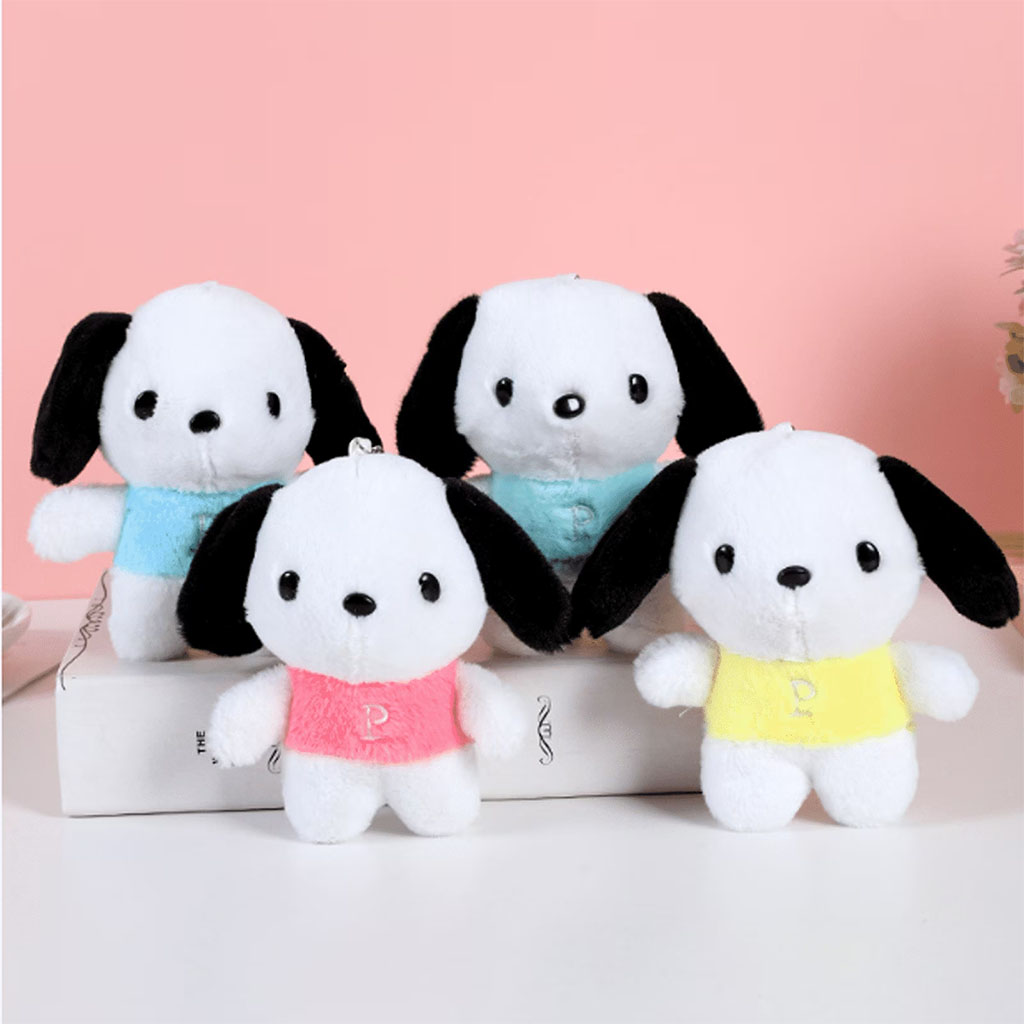 Four small white plush dog toys with black ears wearing colorful shirts in blue, pink, and yellow, displayed on a white surface against a pink background.