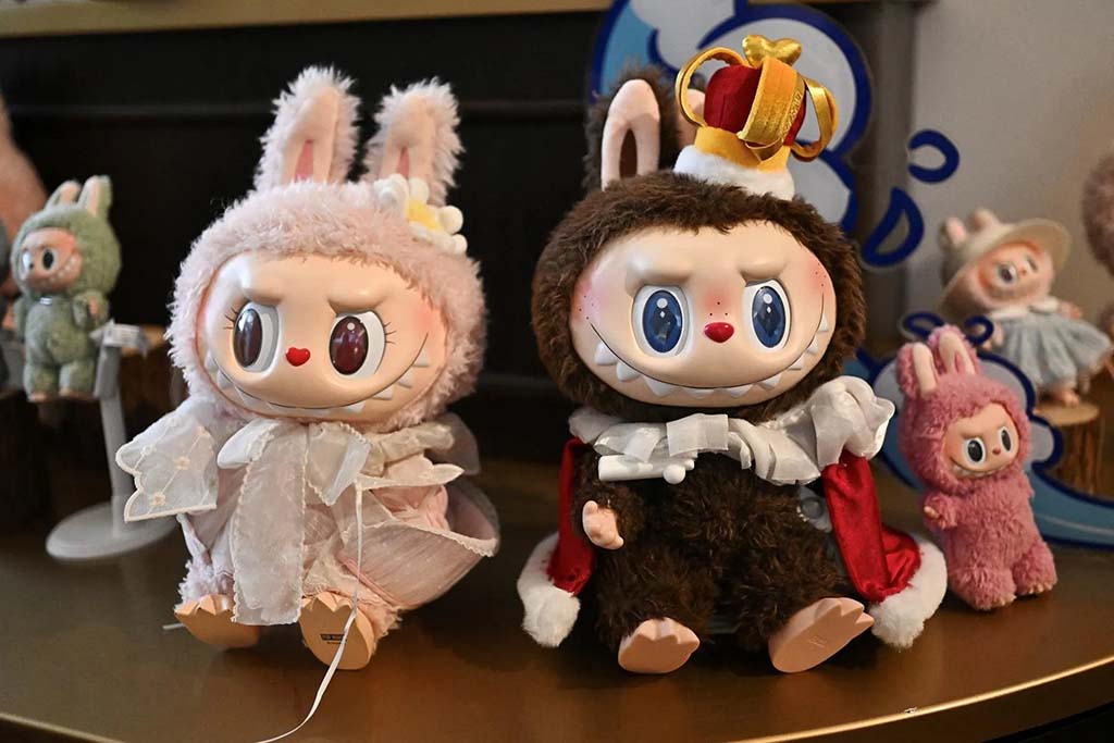 Two Labubu plush dolls dressed in royal and fairy costumes, sitting on a display table with smaller matching figures in the background.