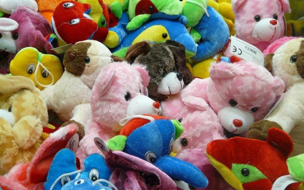 Pile of colorful plush toys including teddy bears, dogs, and other animals made of soft fabrics in pink, blue, red, and yellow.
