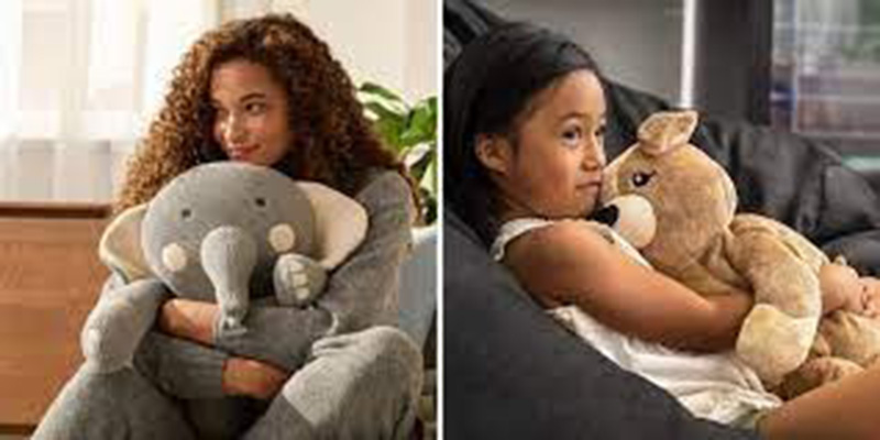 Two people hugging plush toys — one holding a gray elephant plush and the other cuddling a light brown bear plush, both sitting comfortably indoors.